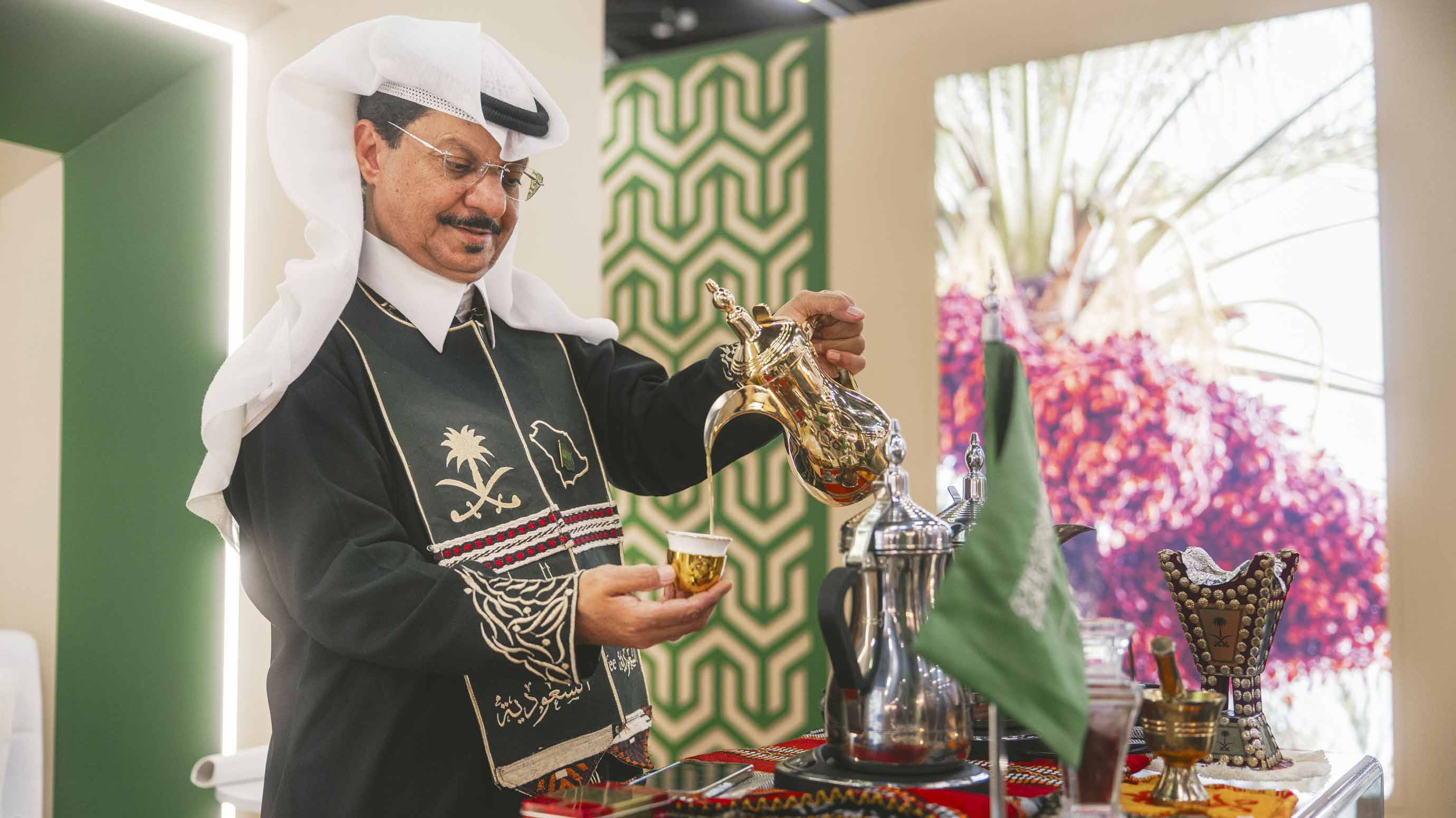 Exhibitor in traditional outfit serves drinks at his booth during the trade fair