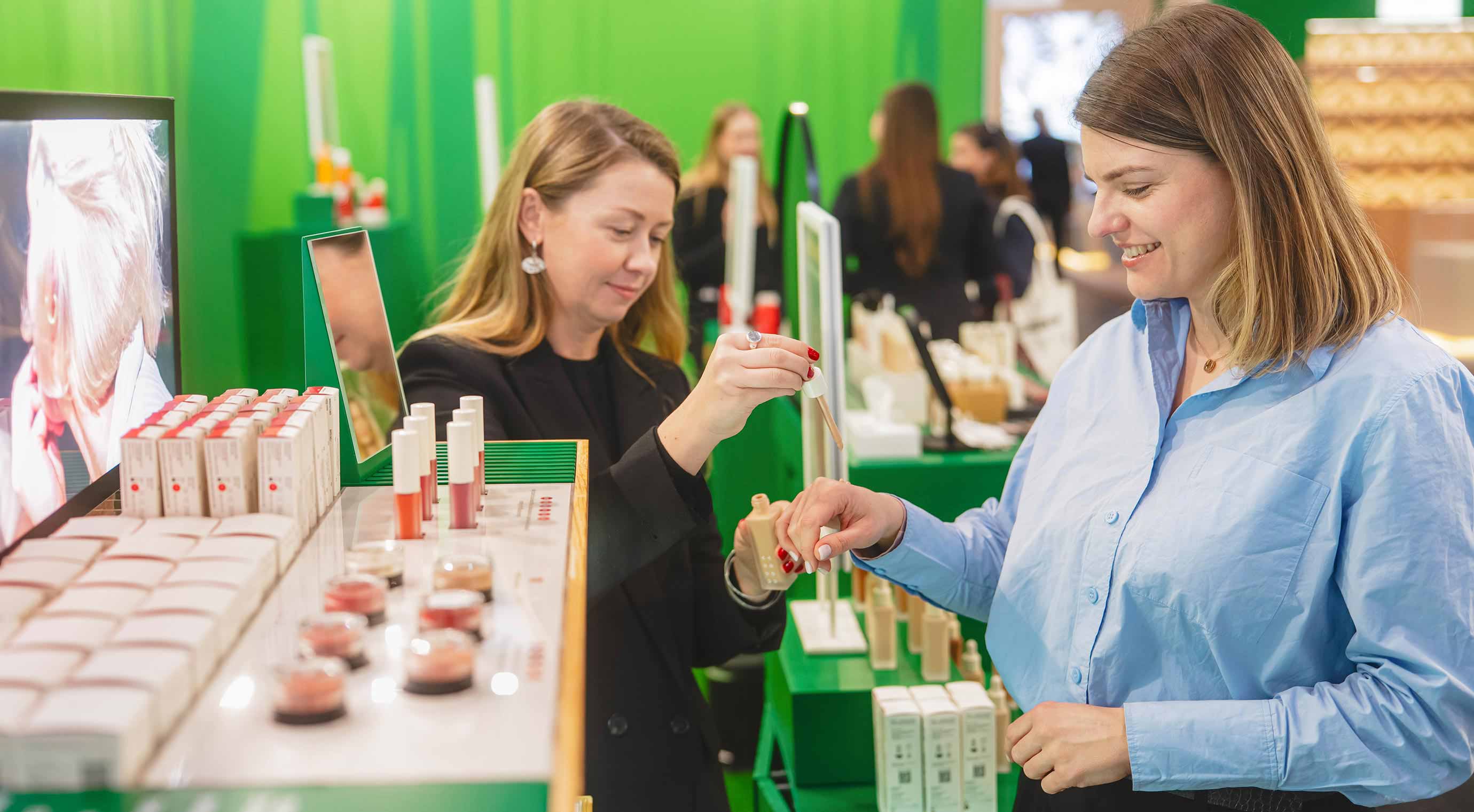 An exhibitor uses a pipette to give a visitor a sample of the cosmetic product to test