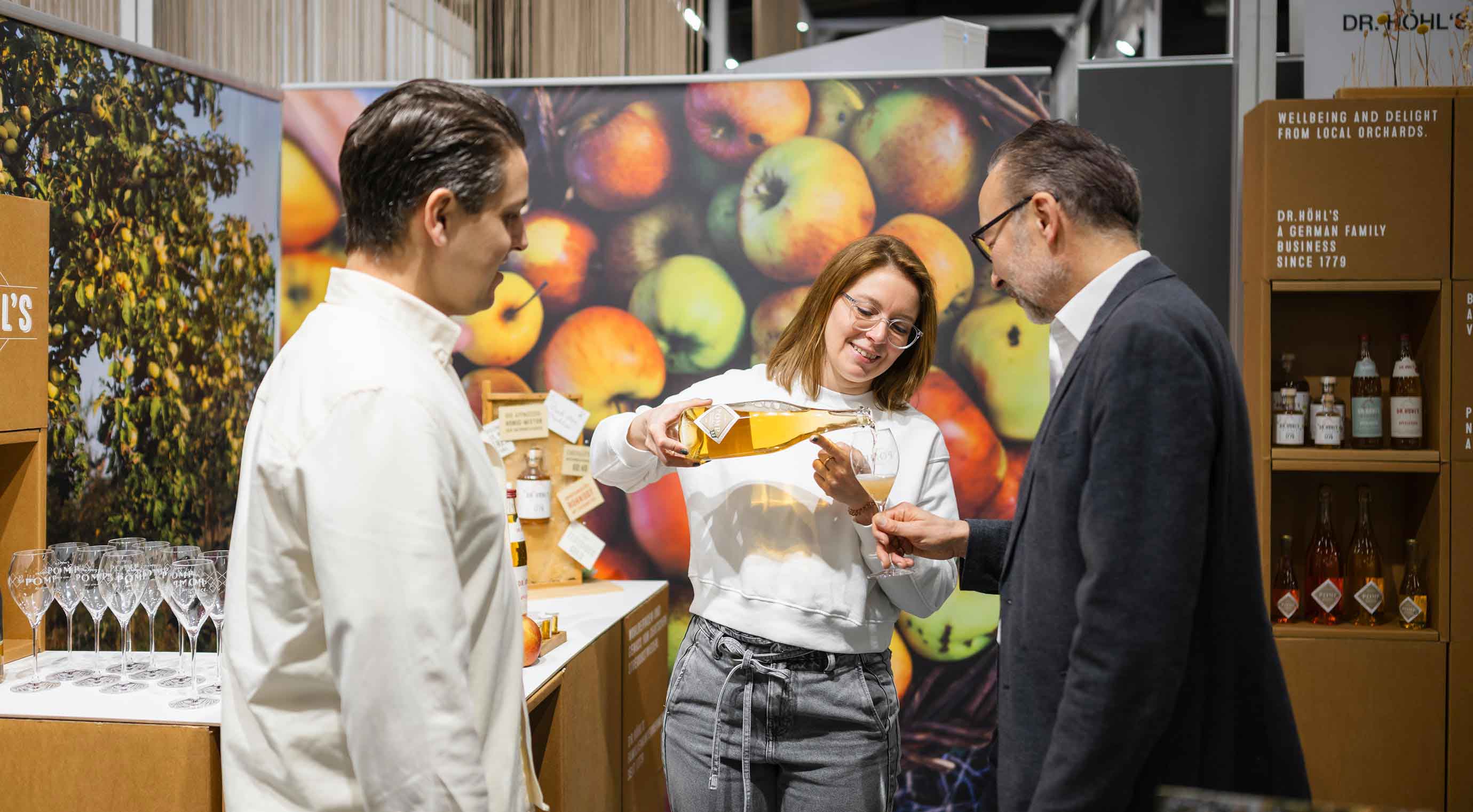 A woman at a stand at the Young Innovators pavilion pours a glass of her product for a visitor